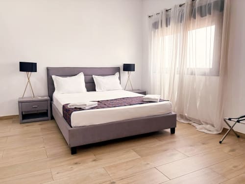 Modern bedroom at DakarByDays apartment with gray upholstered bed, white linens, and sheer curtains in Dakar