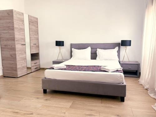 Modern bedroom with gray bed, white pillows, nightstands with black lamps, wooden wardrobe, and parquet flooring at