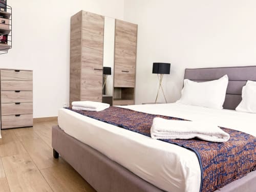 Modern bedroom in DakarByDays apartment with double bed, purple headboard, wooden wardrobe, and white linens in Dakar