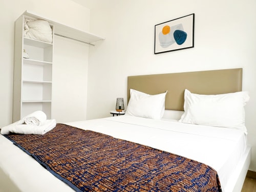 Bright bedroom in DakarByDays apartment with olive headboard, white bedding, patterned throw, and modern wall art in Dakar