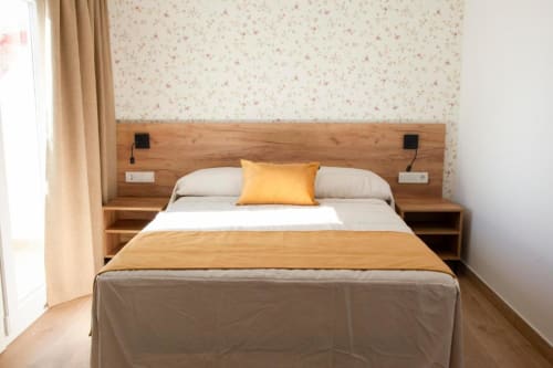 Moderna habitación doble en Hostal Restaurante Angel de Huelma con cama de estructura de madera, papel pintado floral beige y contemporáneo