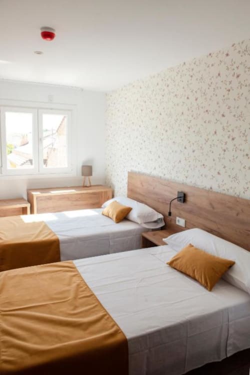 Luminosa habitación doble en Hostal Restaurante Angel con dos camas, cabeceros de madera, almohadas mostaza y papel tapiz floral