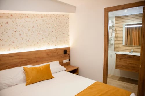 Acogedora habitación en Hostal Restaurante Angel de Huelma con cabecero de madera, almohada amarilla y baño privado.