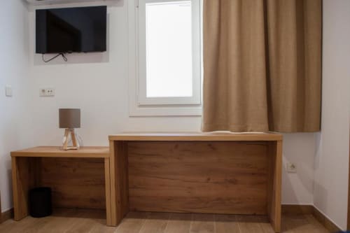 Habitación doble del Hostal Restaurante Angel en Huelma con escritorio de madera, TV de pantalla plana, lámpara de escritorio y cortinas beige