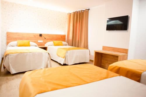 Habitación Cuádruple Superior en Hostal Restaurante Angel de Huelva con múltiples camas, mobiliario de madera y TV de pantalla plana