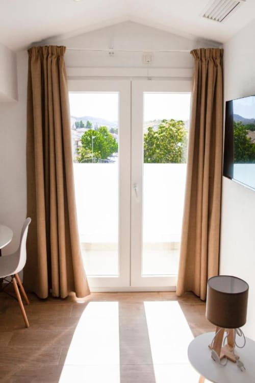 Habitación moderna del Hostal Restaurante Angel en Huelma con puertas de cristal, cortinas beige y vistas a la montaña