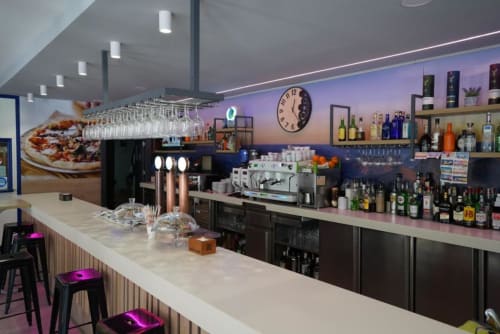 Mostrador de bar moderno en Hostal Restaurante Angel de Huelma con botellas de licores en estantes, cafetera espresso e iluminación ambiente en tonos púrpura
