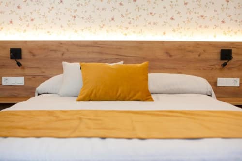 Habitación moderna de Hostal Restaurante Angel con cabecero de madera, ropa de cama blanca y almohadas decorativas amarillas