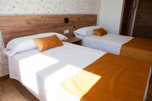 Dormitorio triple en Hostal Restaurante Angel en Huelma con camas blancas, almohadas naranjas y cabecero de madera