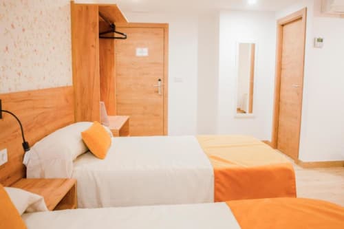 Luminosa Habitación Cuádruple Superior en Hostal Restaurante Angel de Huelva con muebles de madera, ropa de cama blanca y detalles naranjas