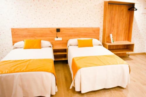 Habitación Cuádruple Superior en Hostal Restaurante Angel de Huelma con dos camas, detalles naranjas y mobiliario de madera