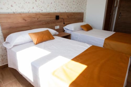 Habitación doble con dos camas, sábanas blancas, almohadas naranjas y cabecero de madera en Hostal Restaurante Angel, Huelma, Jaén