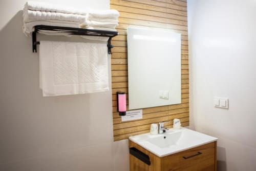 Moderno baño del Hostal Restaurante Angel con tocador de madera, lavabo blanco, espejo, toallero y artículos de aseo en Huelva,