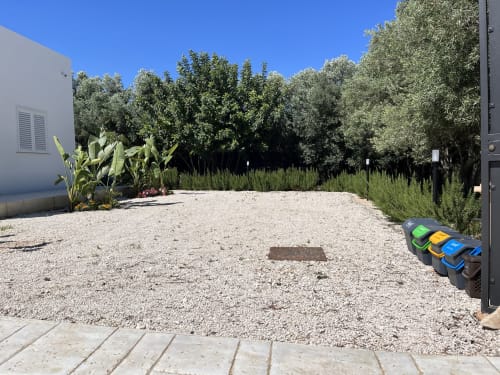 Cortile in ghiaia di Villa Eraklea con bidoni per il riciclaggio, alberi e edificio bianco a Noto, Sicilia