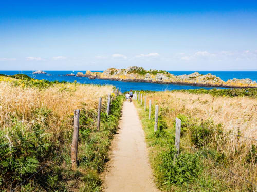Sentier côtier sablonneux bordé de poteaux en bois menant vers la baie turquoise et les îlots rocheux près de L'Échappée Baie, Roz-sur-Couesnon