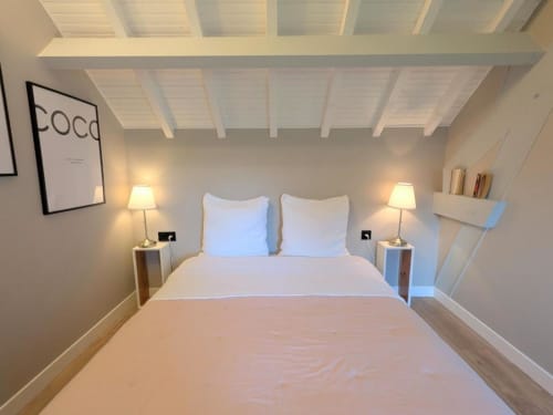 Chambre moderne et lumineuse avec literie blanche, poutres apparentes, lampes jumelées et art mural au Clos d'Émilie B&B en France
