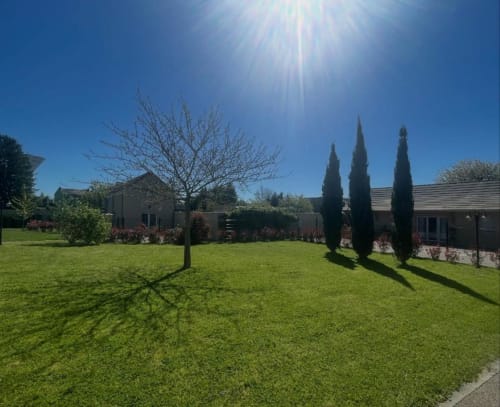 Le jardin paysager du Clos d'Émilie avec pelouse soignée, cyprès et architecture contemporaine sous ciel bleu