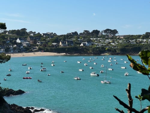 Baie turquoise avec bateaux amarrés, plage de sable fin et charmant village côtier de Roz-sur-Couesnon
