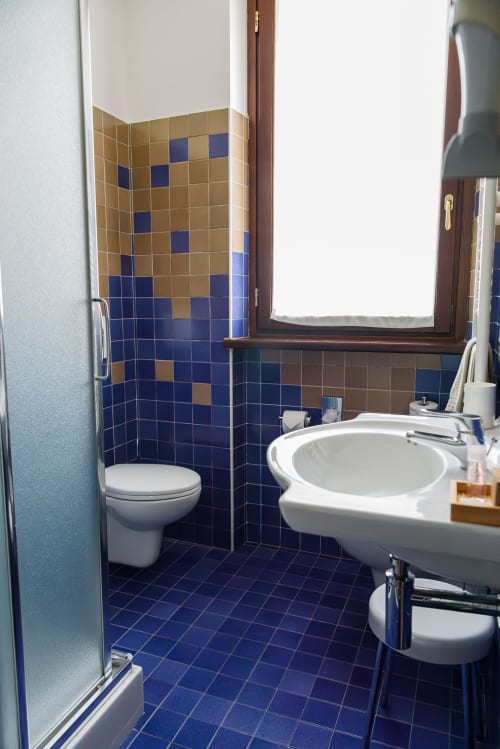 Bagno della camera Classic dell'Hotel FortyFive a Chivasso con piastrelle blu e beige, lavandino e wc bianchi, e finestra.