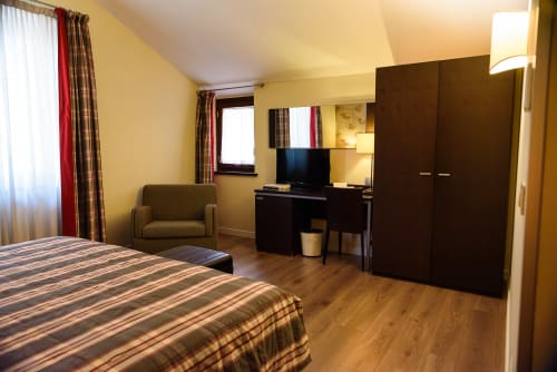 Camera superiore presso l'Hotel FortyFive a Chivasso con letto, poltrona, scrivania, TV e arredi in legno scuro