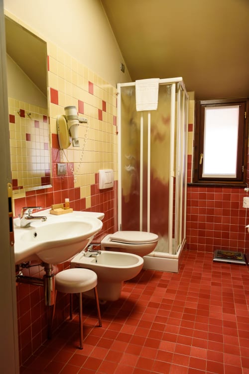 Bagno superior dell'Hotel FortyFive a Chivasso con pavimento in piastrelle rosse, pareti gialle, doccia, wc e bidet.