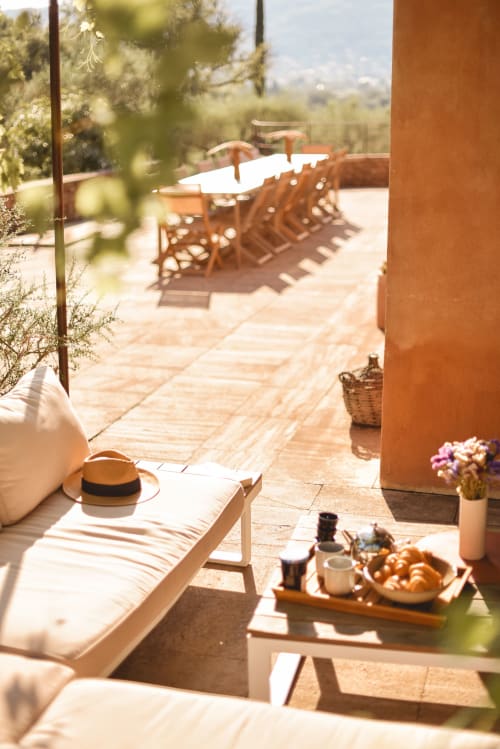 Terrasse ensoleillée des Hauts de Diane avec table dressée, chapeau de paille, croissants et vue sur le jardin à Cuers