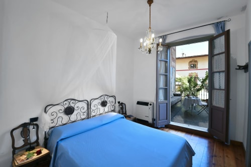 Camera da letto luminosa con copriletto blu, letto in ferro battuto ornato, lampadario di cristallo e porte-finestre che si affacciano sulle montagne
