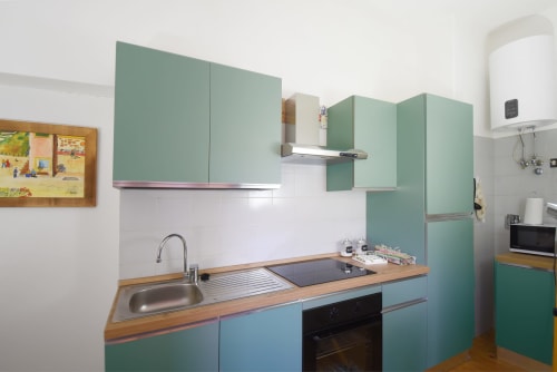 La cucina moderna ed interamente attrezzata della Suite Drago al Roseto del Drago (Ponte in Valtellina, Sondrio), dotata di piano a induzione, forno, frigorifero e decorata con quadri naïf di Marialuisa Cassan.