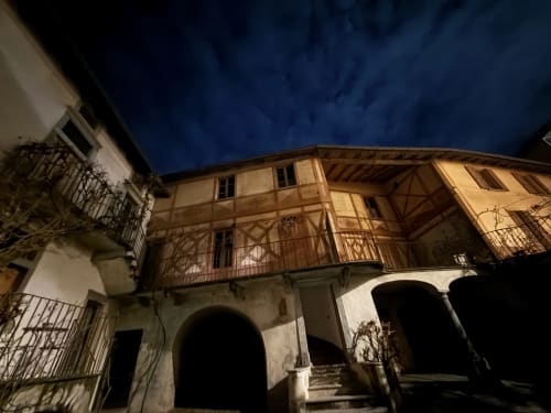 Affascinante scorcio notturno del cortile interno e della facciata decorata a trompe-l'œil con finto legno al Roseto del Drago a Ponte in Valtellina (Sondrio), illuminato sotto il cielo stellato.