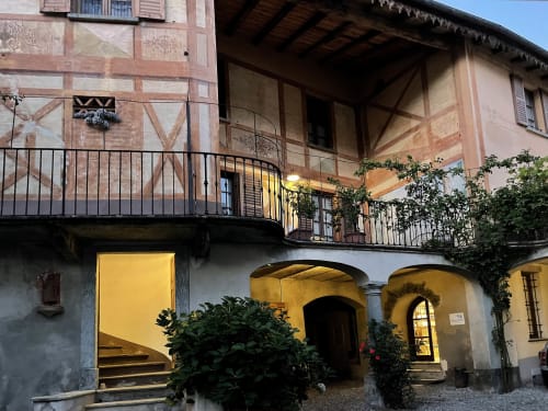 Caratteristico cortile interno del Roseto del Drago a Ponte in Valtellina (Sondrio), con elegante porticato in pietra, piante fiorite e facciata storica decorata a trompe-l'œil effetto finto legno.