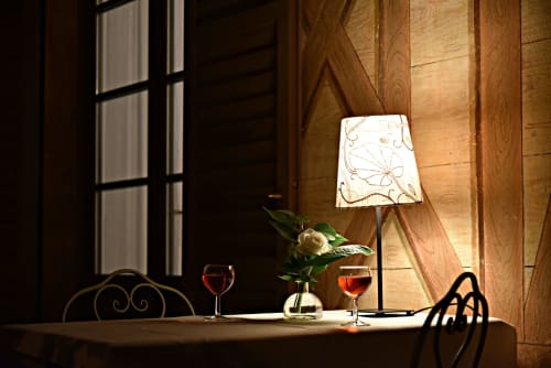 Un'intima e romantica atmosfera serale sul terrazzo coperto della Suite Drago al Roseto del Drago (Ponte in Valtellina, Sondrio): tavolo apparecchiato con lampada da tavolo, fiori freschi e calici di vino della Valtellina.