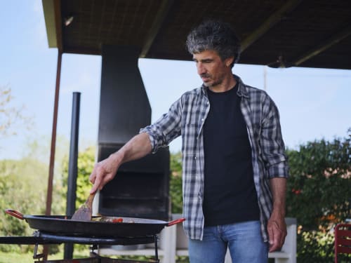 Hombre cocinando en la parrilla exterior de la villa Can Serrà 1786 en Llagostera, España, con vistas a las montañas