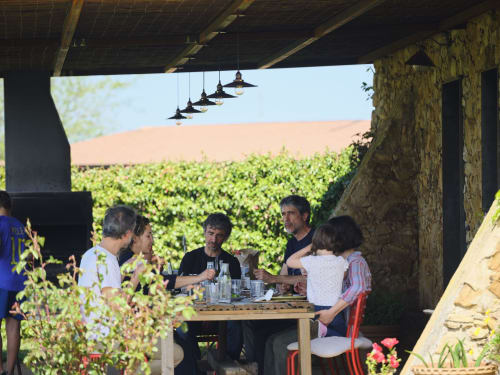 Huéspedes cenando juntos bajo una pérgola en la villa Can Serrà 1786 en Llagostera con vistas a los viñedos