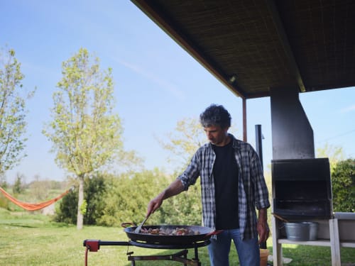 Hombre haciendo una barbacoa en la villa Can Serrà 1786 en Llagostera, con vistas a las montañas y árboles