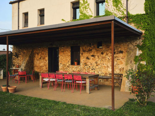 Terraza de piedra rústica en la villa Can Serrà 1786 en Llagostera con sillas rojas y mesa de madera bajo pérgola