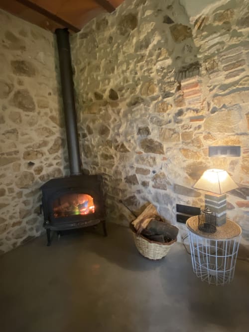 Chimenea de piedra acogedora con estufa de leña encendida, lámpara y cestas de mimbre en el salón de la villa Can Serrà 1786, Llagostera