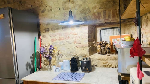 Cocina rústica en la villa Can Serrà 1786 de Llagostera con muros de piedra, iluminación colgante, electrodomésticos y barra comedor