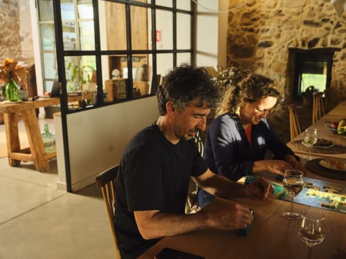 Dos comensales cenando en una mesa de madera en la villa Can Serrà 1786 en Llagostera, España, con muros de piedra e interior moderno.