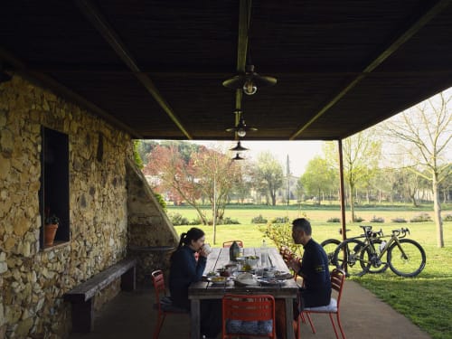 Dos huéspedes cenando bajo una terraza cubierta en la villa Can Serrà 1786 en Llagostera con bicicletas y vistas al campo.