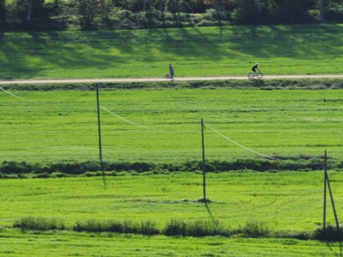 Ciclista en camino rural con verdes campos y pastos vallados en Can Serrà 1786 en Llagostera