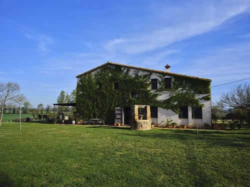 Villa rural catalana Can Serrà de 1786 en Llagostera rodeada de campos verdes y muros de piedra cubiertos de hiedra