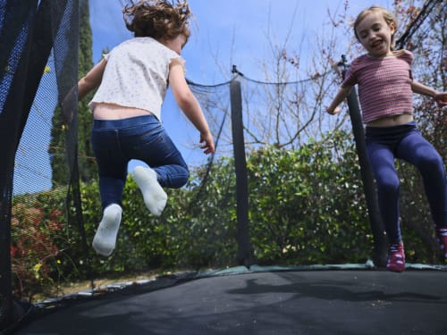 Dos niños pequeños saltando en una cama elástica en la villa Can Serrà 1786 en Llagostera, con vistas a las montañas y jardín.