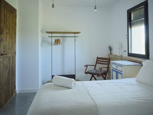 Dormitorio luminoso en la villa Can Serrà 1786 de Llagostera con ropa de cama blanca, armario de madera y vistas a las montañas
