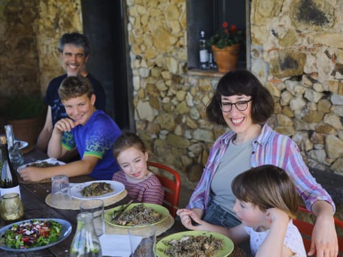 Familia cenando junta en la villa Can Serrà 1786 en Llagostera, disfrutando de una comida con muros de piedra de fondo.