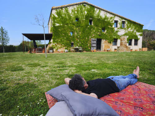 Huésped relajándose en el jardín de la villa Can Serrà 1786 en Llagostera con edificio de piedra cubierto de hiedra y jardines
