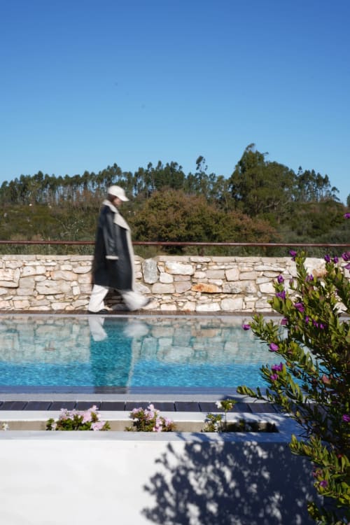 Personne se promenant près de la piscine immaculée de l'hôtel de luxe Recantos D'Almerinda à Pombal, avec vue sur les murs en pierre et la forêt