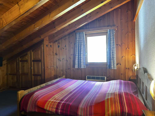 Chambre alpine rustique à l'Hôtel les Bouquetins à Zinal avec literie à rayures colorées et vue montagnarde par la fenêtre