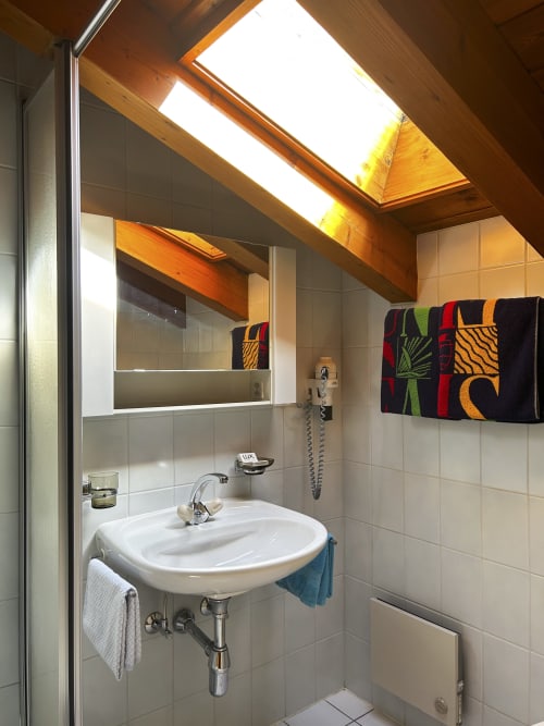 Salle de bain moderne à l'Hôtel les Bouquetins, Zinal, avec lavabo blanc, puits de lumière, serviettes colorées et murs carrelés