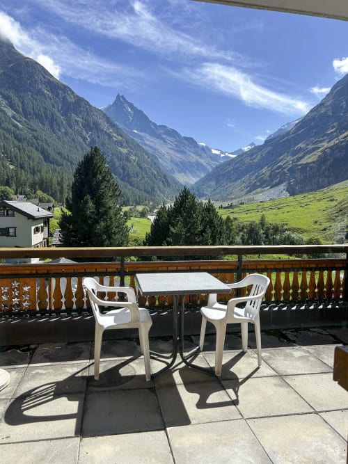 Chaises et table blanches sur la terrasse ensoleillée de l'Hôtel les Bouquetins à Zinal, avec vue sur les Alpes et la vallée verdoyante
