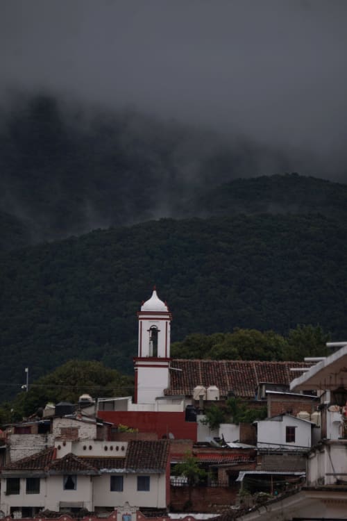Torre de iglesia colonial en San Cristóbal de las Casas elevándose sobre montañas brumosas y arquitectura tradicional